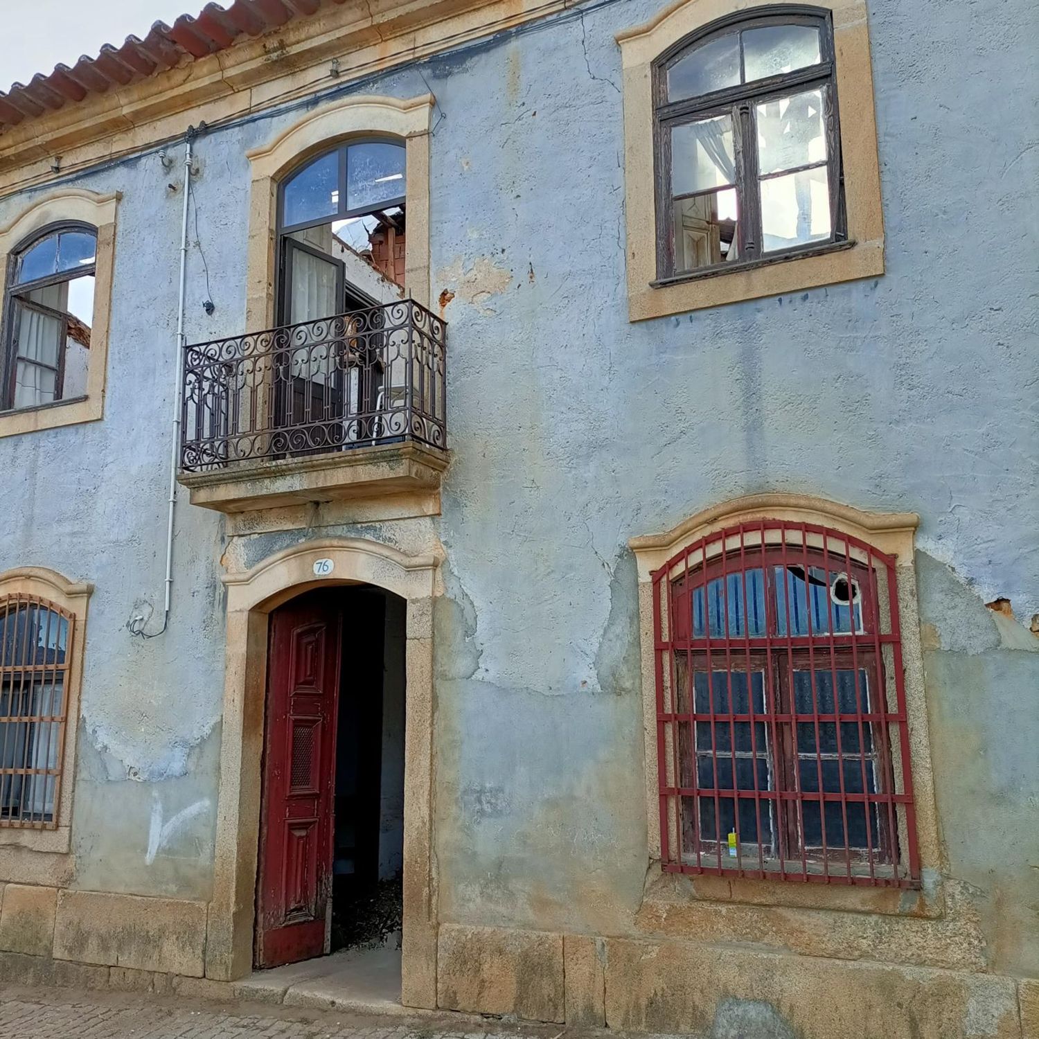 A fachada antes da obra, com reboco azul a cair e janelas partidas