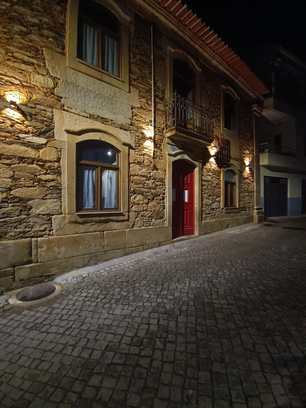 A fachada de pedra da casa à noite, com a porta vermelha iluminada